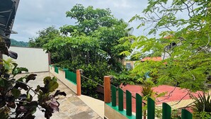 A tiled outdoor area with a green railing, trees, and a building in the background.