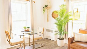 A room with a round glass table, two chairs, a potted plant, a radiator, and a brown leather sofa. - Sweet Stowe Apartment (Stowe)