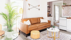A modern living room with a brown leather sofa, a glass table, a round coffee table, and a patterned rug. - Sweet Stowe Apartment (Stowe)