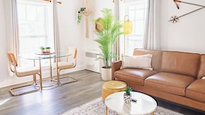 A living room with a brown leather sofa, a glass coffee table, a round dining table with chairs, and a potted plant. - Sweet Stowe Apartment (Stowe)
