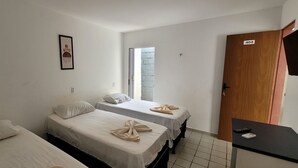 A room with two beds, a wooden door, a small table with a remote, and a window. - Pousada Primeiro Sol (João Pessoa)