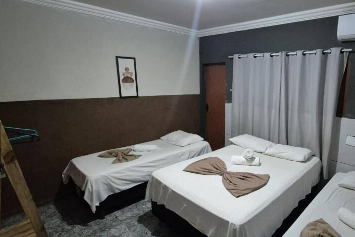 A hotel room with two single beds, a wooden chair, a framed picture on the wall, and an air conditioning unit.