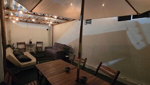 A cozy patio area with a wooden table, cushioned seating, and a ceiling with exposed beams and string lights. - Pousada Primeiro Sol (João Pessoa)