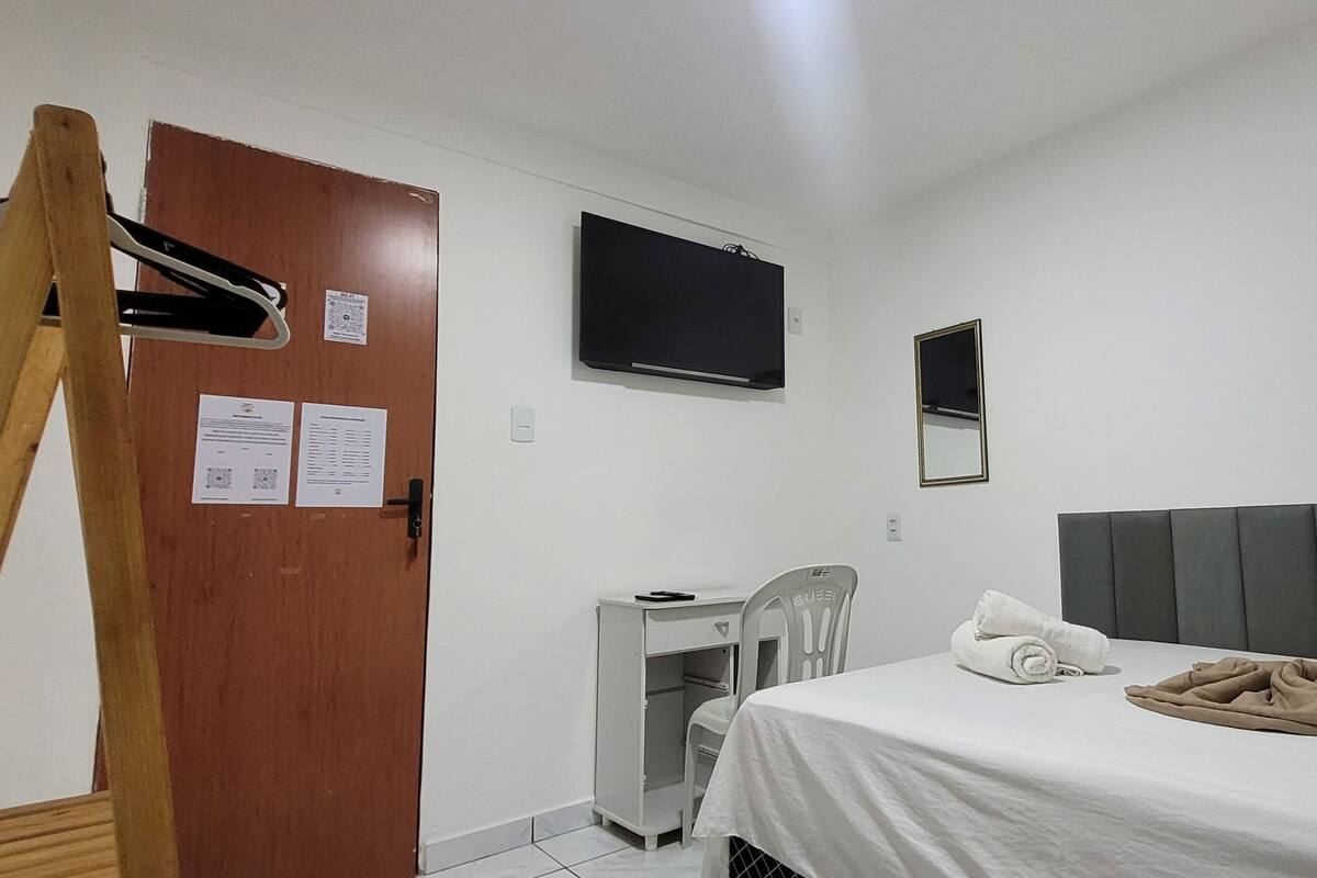 A hotel room with a bed, a desk, a chair, a television, and a door.