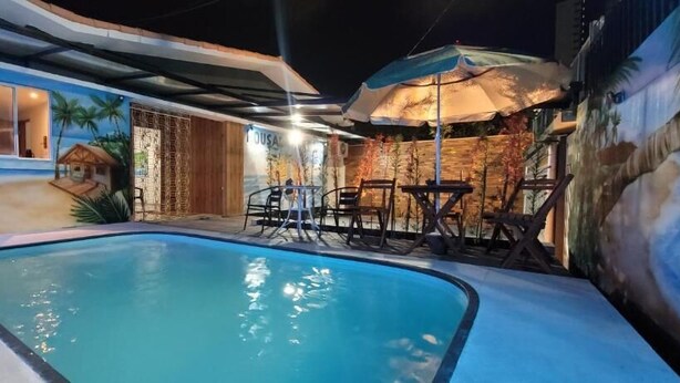 A swimming pool with lounge chairs and umbrellas, surrounded by a mural of a beach scene. - Pousada Primeiro Sol (João Pessoa)