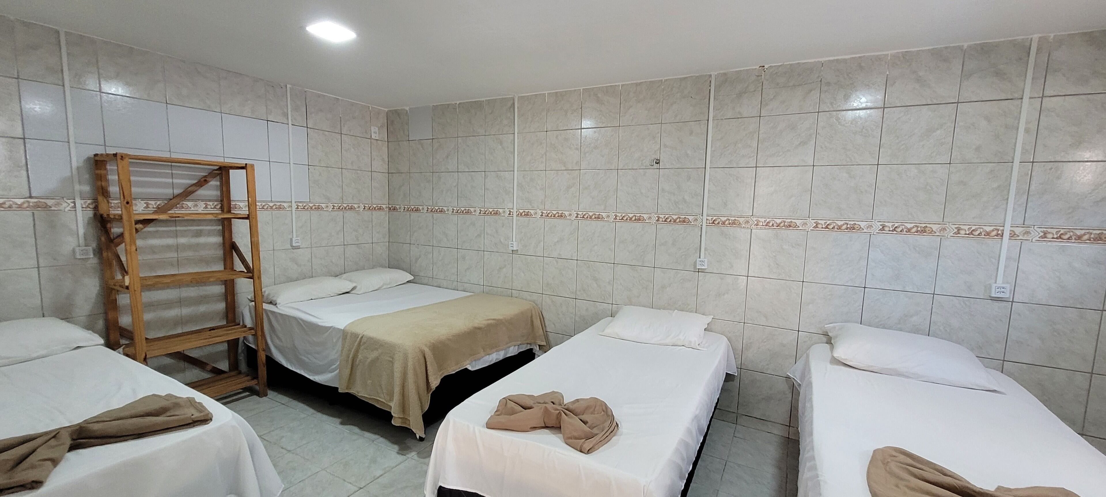 A hotel room with three single beds, a wooden shelf unit, and tiled walls.