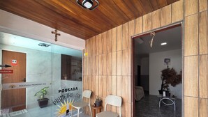 A reception area with a wooden wall, a glass door, and a sign indicating a first-floor location. There are two chairs and a small table with a potted plant. - Pousada Primeiro Sol (João Pessoa)