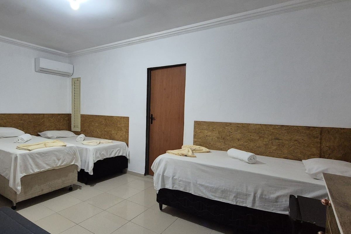 A hotel room with three single beds, a wooden headboard, a door, and an air conditioning unit.
