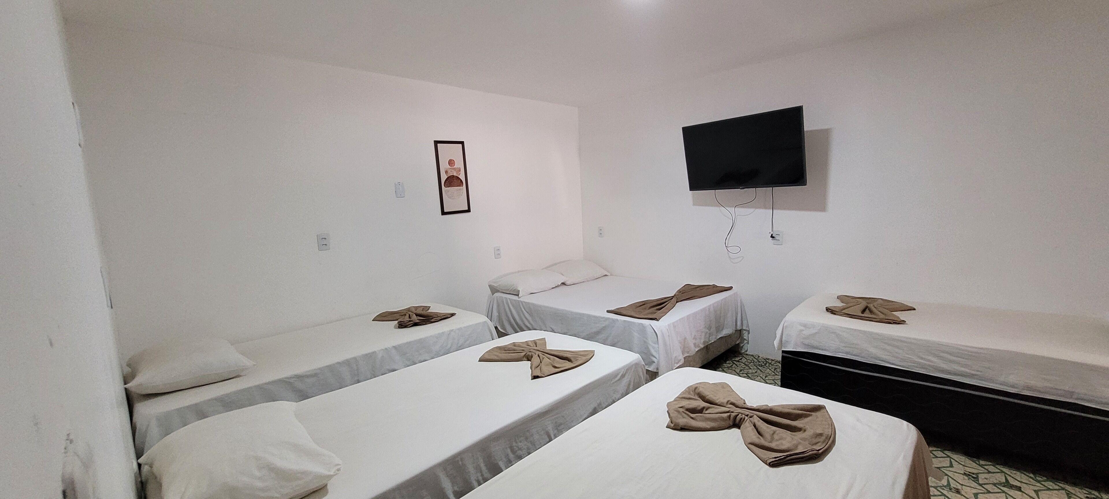Une chambre d’hôtel avec quatre lits simples, un téléviseur à écran plat fixé au mur et un tableau encadré accroché au mur.