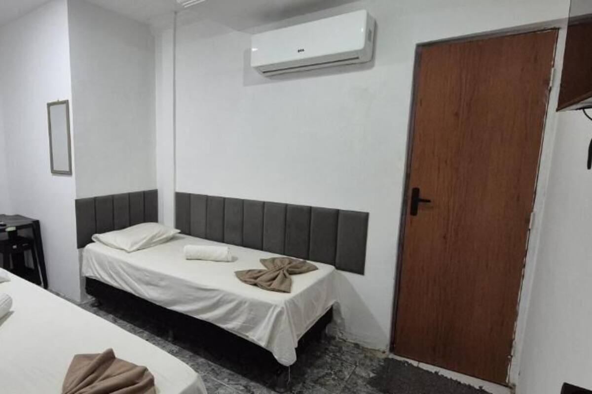 A room with two beds, a wooden wardrobe, a small table, and an air conditioning unit.