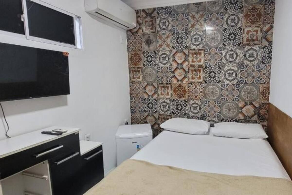 A bedroom with a bed, a desk, a chair, a TV, and a patterned wall.