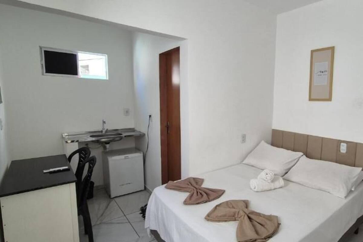 A hotel room with a bed, a desk, a small kitchenette, and a mirror.