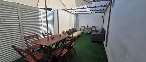 Un patio con una mesa y sillas de madera, un sofá gris y una mesita con una planta en maceta.