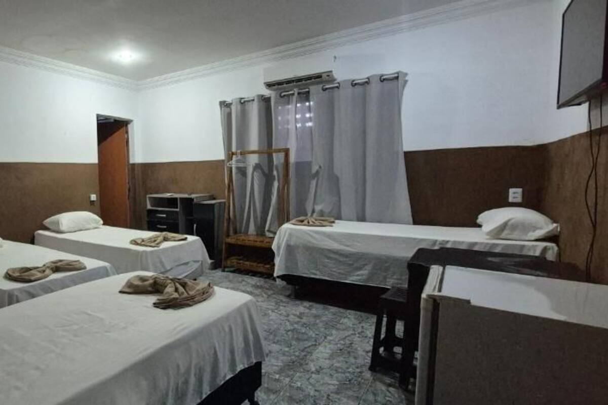 A hotel room with four single beds, a desk, a chair, a TV, and a window with curtains.