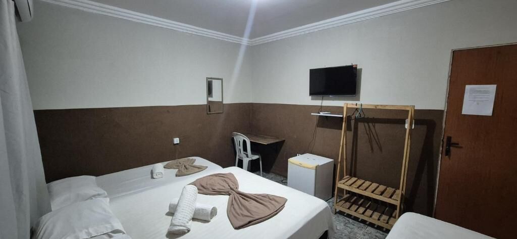 A hotel room with a bed, a desk, a television, and a wooden wardrobe.
