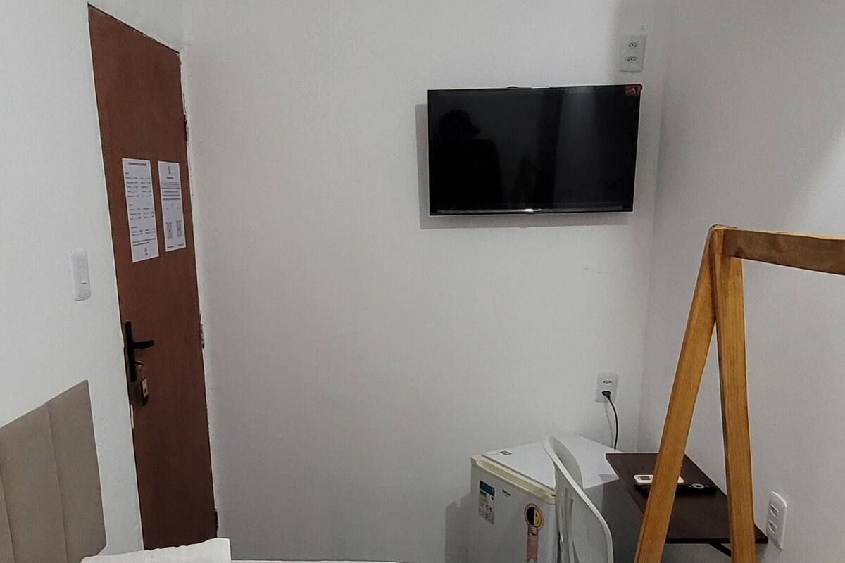 A hotel room with a bed, a desk, a TV, and a wooden bench.