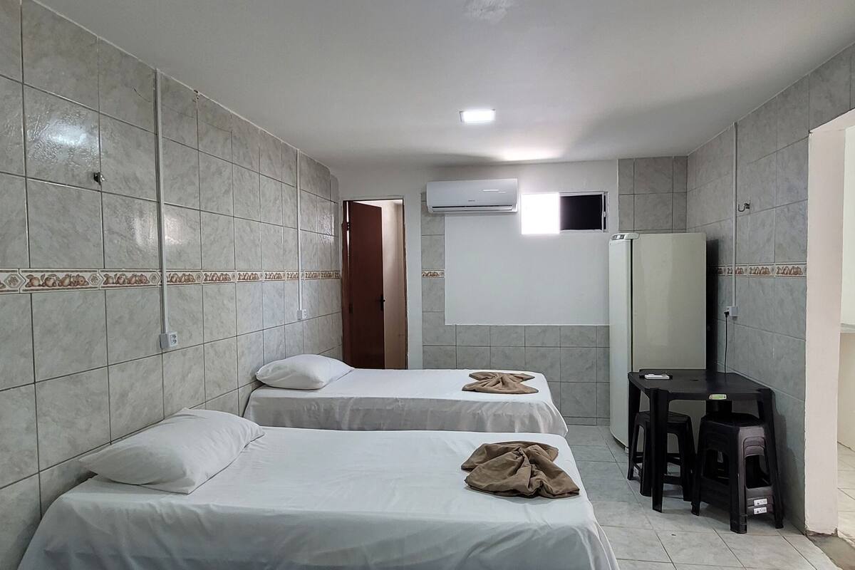 A hotel room with two beds, a TV, a small table, and an air conditioning unit.