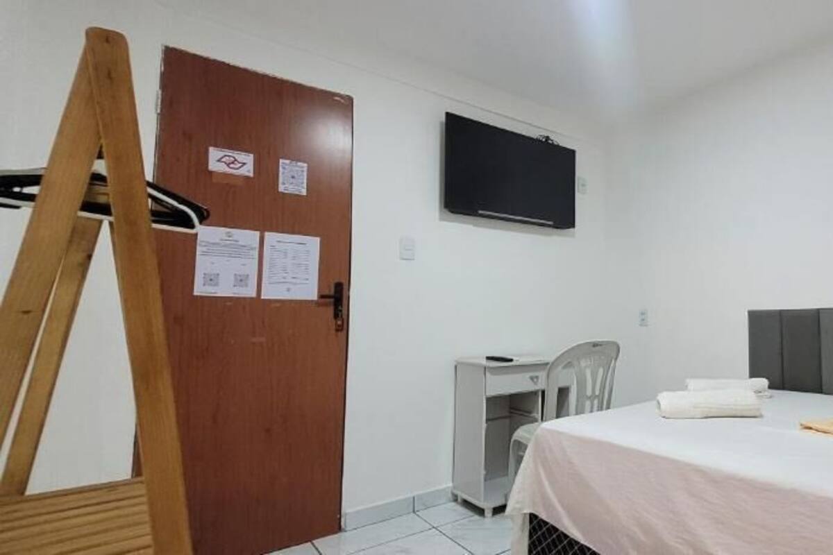 A room with a bed, a desk, a chair, a television, and a wooden door.