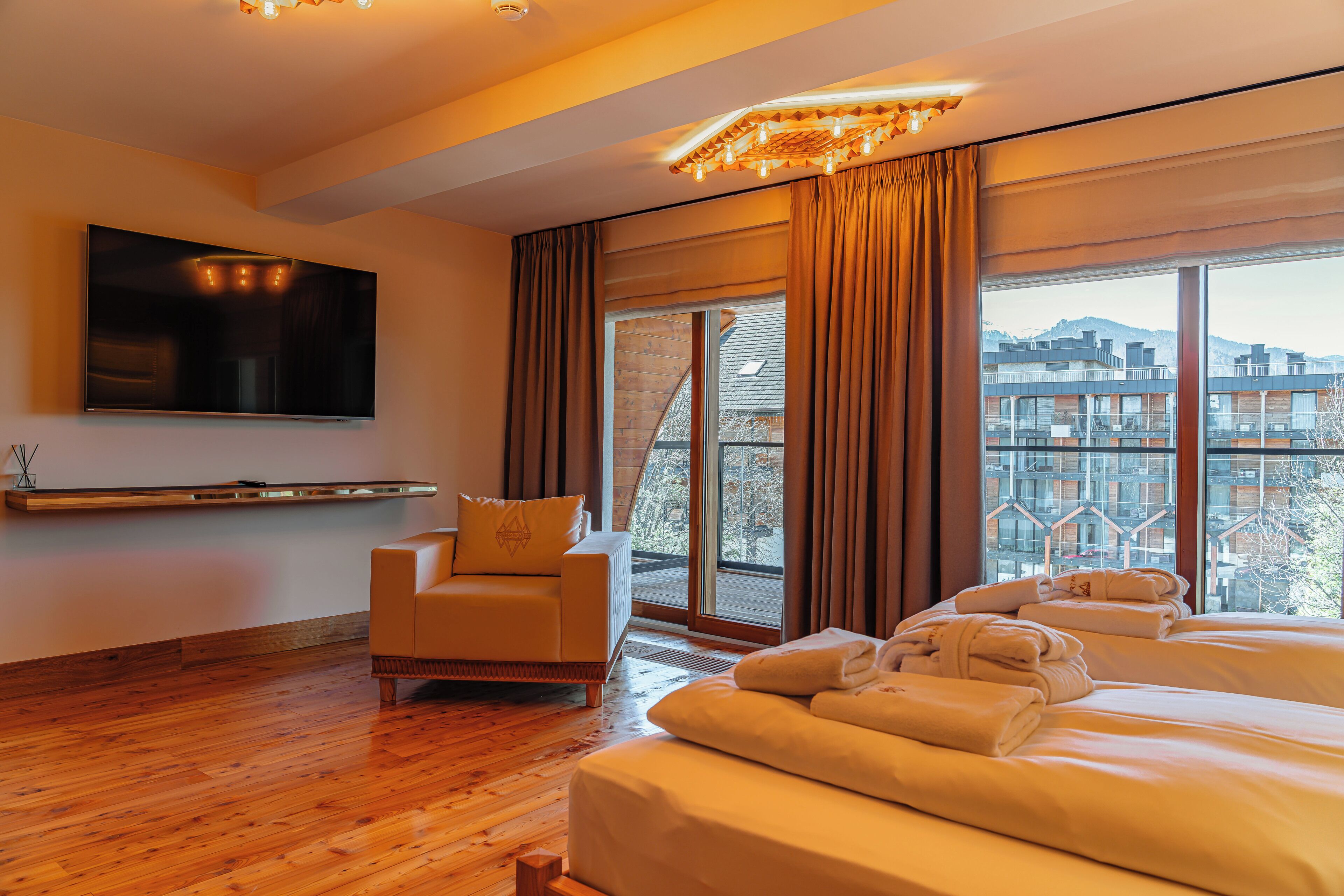 A hotel room with a large bed, a sofa, a TV, and a view of buildings through the window.