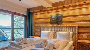 A hotel room with a large bed, wooden paneling, a painting above the bed, and a window with a view of trees. - Mountain Diamond Resort (Zakopane)