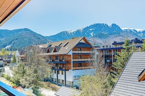 Un edificio de varios pisos con balcones, fachada de madera y montañas al fondo.
