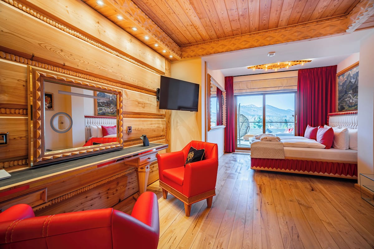 Ein Zimmer mit Holzwänden, einem Bett, einem Fernseher, einem Spiegel und einem roten Sessel.