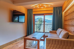 Una sala moderna con sofá, una mesa, televisor montado en la pared y un ventanal con vistas a las montañas.