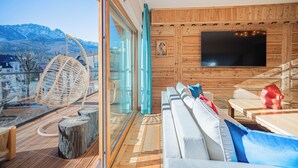 A modern interior with a sofa, wooden flooring, a television, and a view of mountains. - Mountain Diamond Resort (Zakopane)