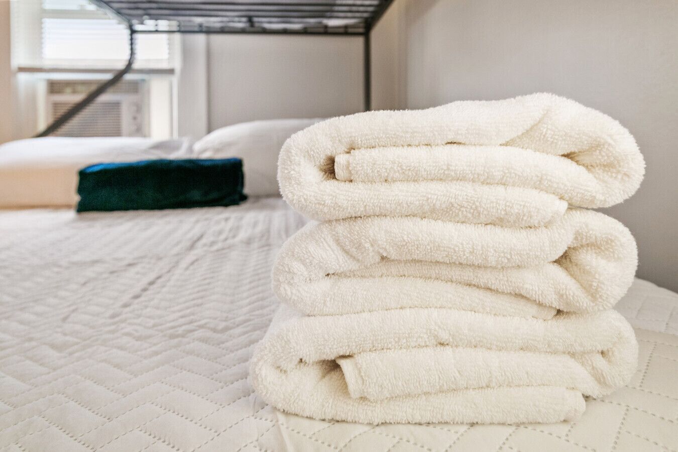 Une serviette blanche, soigneusement pliée, est posée sur le lit, recouvert d’une courtepointe blanche.