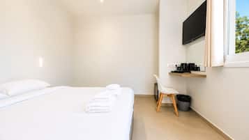 Una habitación de hotel moderna con una cama, una silla, un televisor y un estante pequeño con objetos.