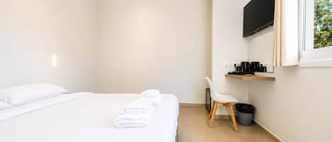Ein modernes Hotelzimmer mit einem Bett, einem Sessel, einem Fernseher und einer kleinen Ablage mit Gegenständen.