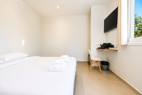 A modern hotel room with a bed, a chair, a TV, and a small shelf with items.