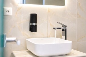 Un baño con un lavamanos blanco, un grifo moderno y un dispensador de jabón montado en la pared.