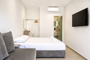 A modern hotel room with a bed, a seating area, a TV, and a bathroom visible through an open door. - Sea And Sky Near Athens Airport By SEM (Spata-Artemida)