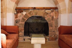 Ein Kamin aus Stein mit einer Glasablage, zwei Sofas und einem kleinen Tisch in einem Raum mit Fliesenboden.