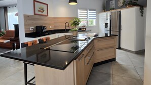 Een moderne keuken met een groot eiland, hanglampen en een koelkast.