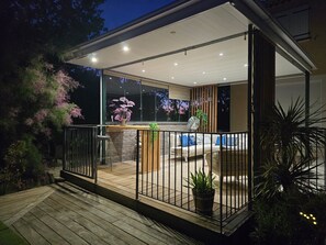 An outdoor patio area with a wooden deck, a seating area with cushions, and a potted plant. - Villa “Superb With Pool” with Private Pool, Wi-Fi, and Cooling Floor System (Bras)