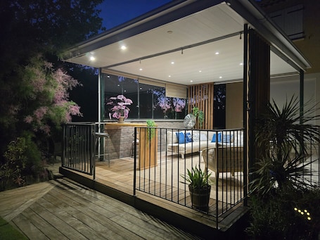An outdoor patio area with a wooden deck, a seating area with cushions, and a potted plant.