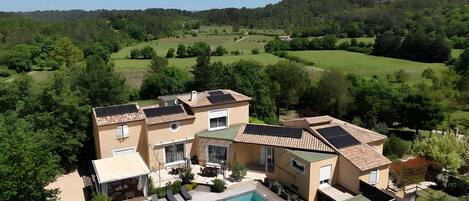A two-story house with a swimming pool, surrounded by greenery and hills.