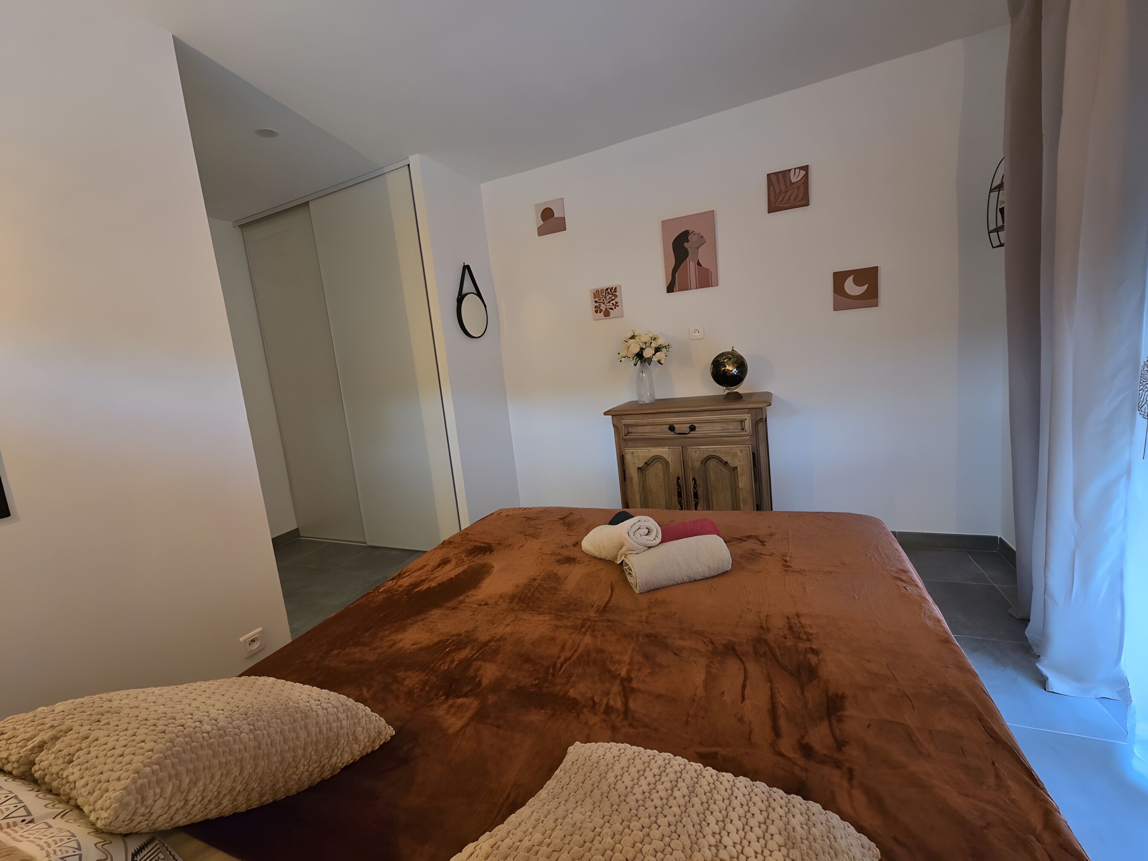 A room with a large bed, a wooden dresser, and a door leading to another room.