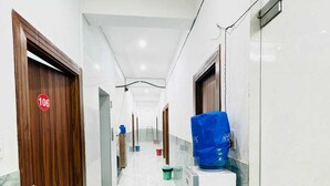 A hotel corridor with a wooden door marked '106', a white wall, a blue bag on a counter, and a green mat on the floor. - Hotel Vrinda Nikunj Dham (Vrindavan)