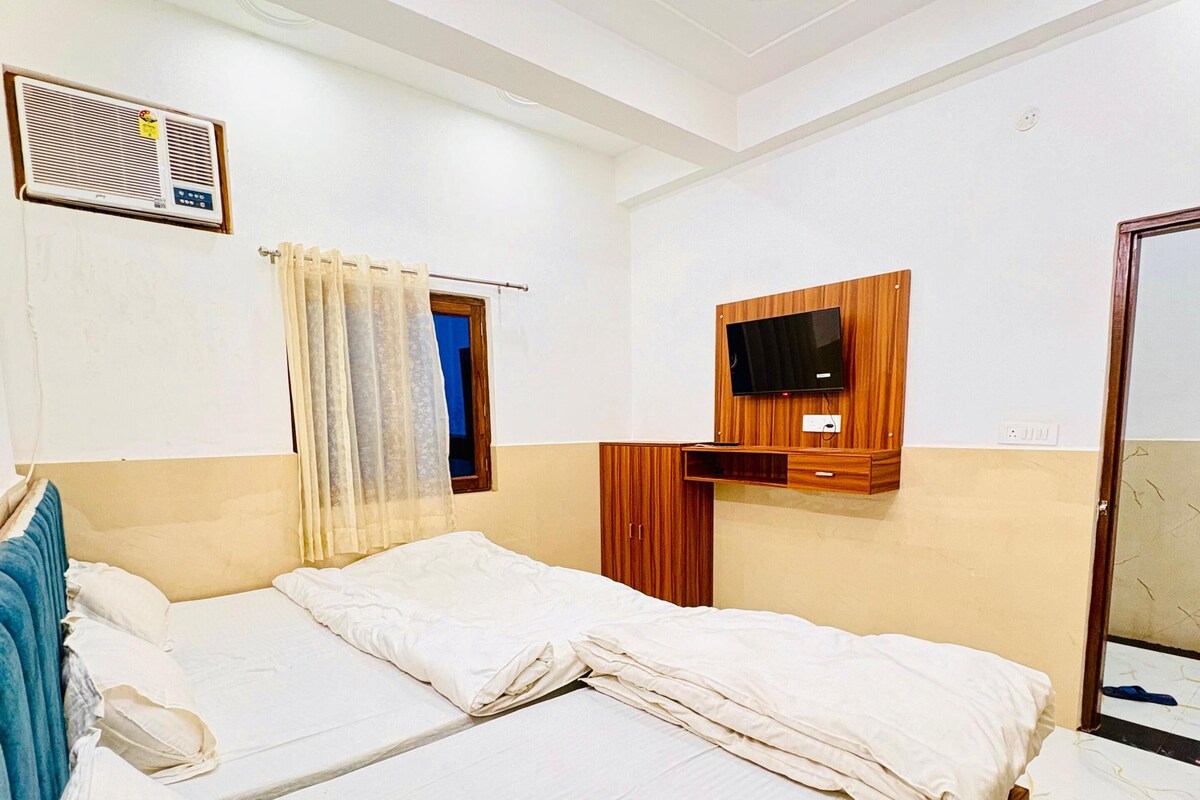 Une chambre d’hôtel avec un lit, un ventilateur de plafond, un téléviseur fixé au mur et une fenêtre avec des rideaux.