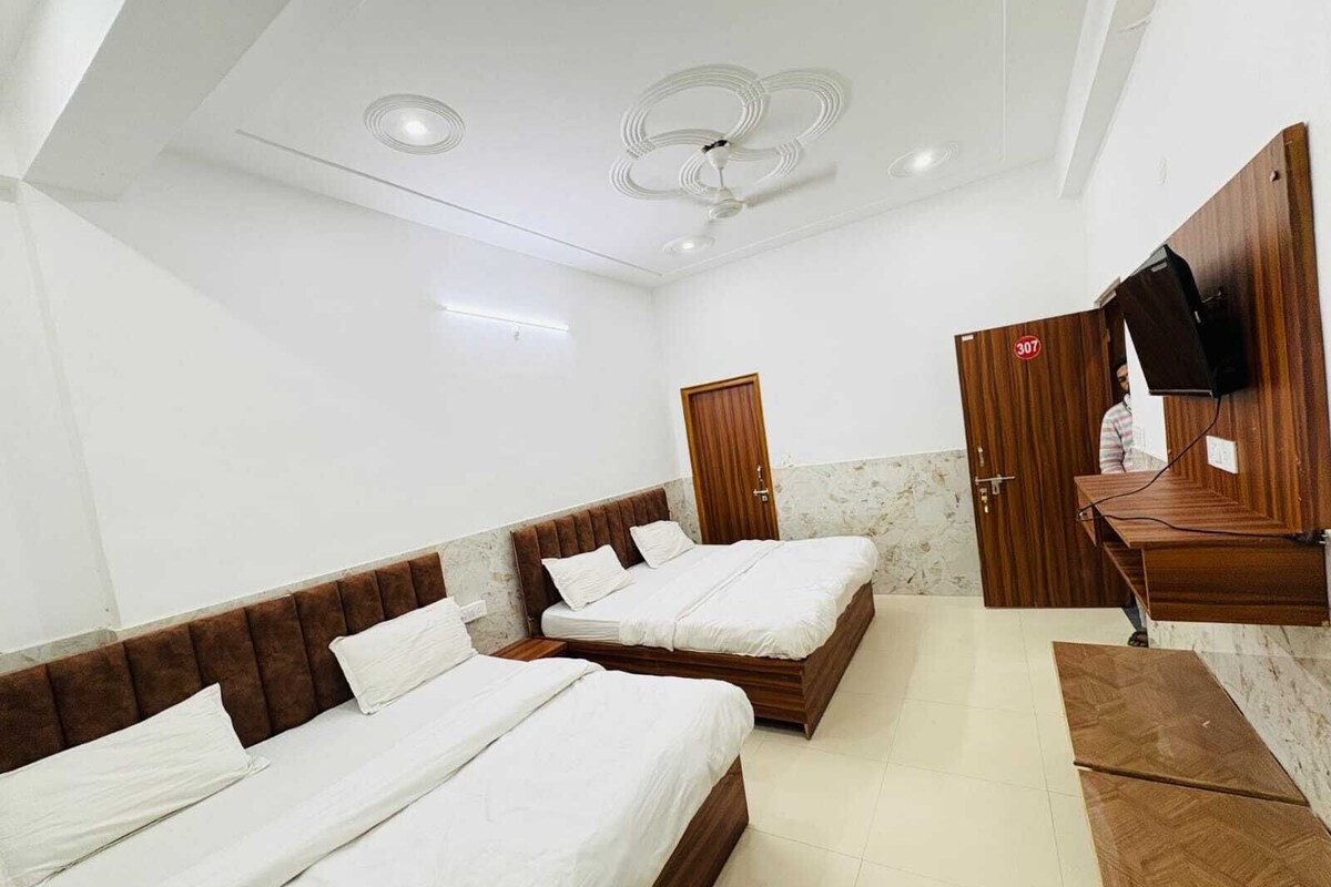 Une chambre d’hôtel avec deux lits, une tête de lit en bois, un ventilateur de plafond, un téléviseur fixé au mur et un bureau en bois.