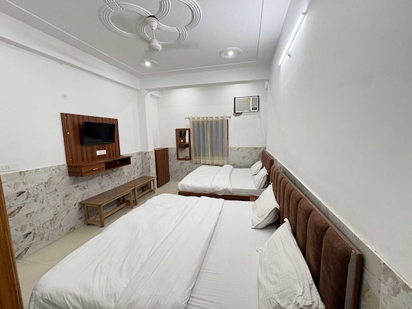 Une chambre d’hôtel avec deux lits, une télévision, un miroir, un banc et un ventilateur de plafond.