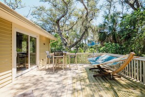 Eine Holzterrasse mit einer Hängematte, einem Tisch mit Stühlen und einer Glastür, die auf eine Terrasse führt.