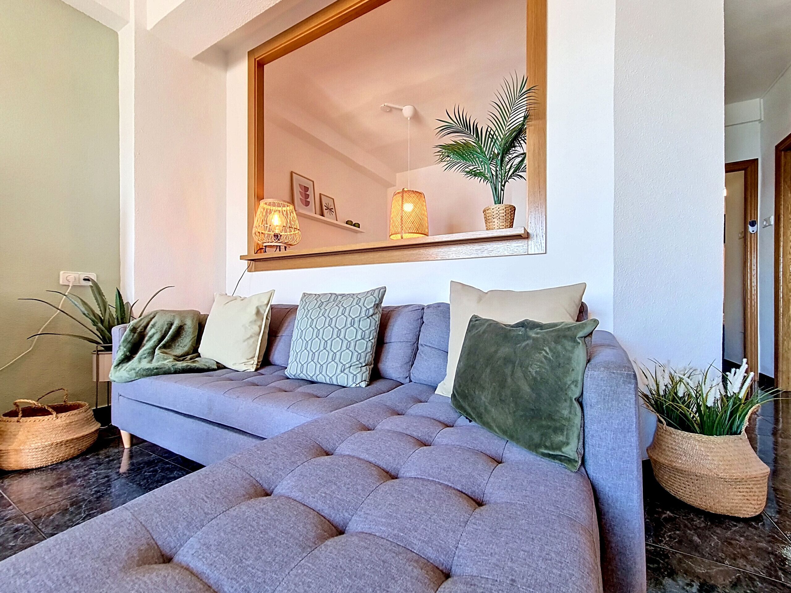 A modern living room with a grey sofa, a large mirror, and decorative plants.