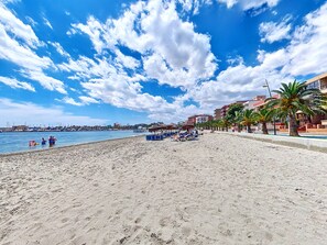 Ein Strand mit blauem Himmel, Palmen und einer Reihe von Liegestühlen.