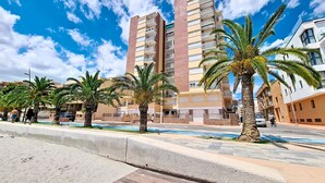 Um edifício de vários andares com varandas, palmeiras e céu claro.