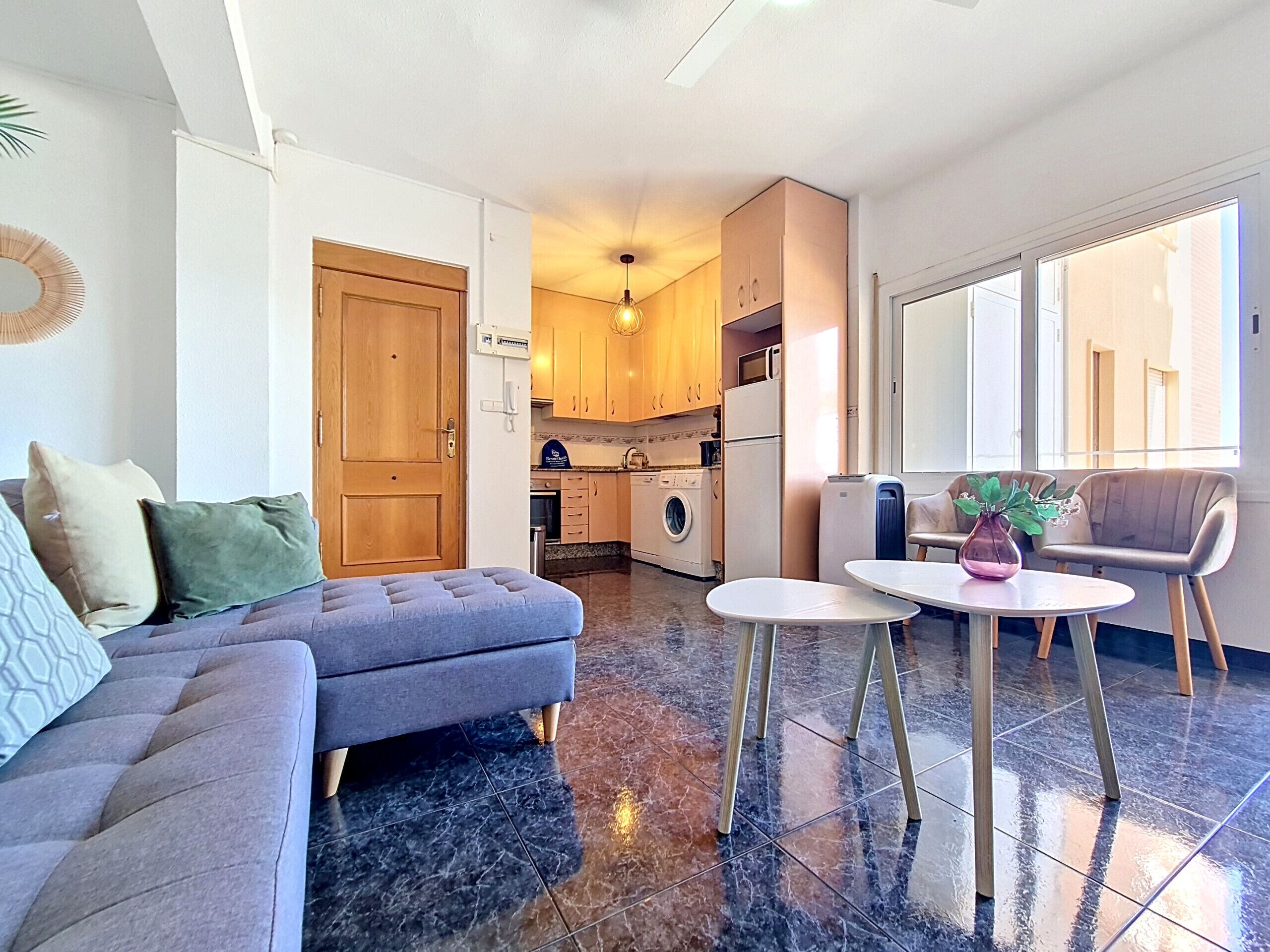 A compact living space with a sofa, a dining table, a kitchen area, and a large window.