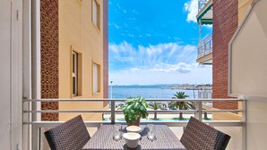 Varanda com mesa e cadeiras, planta em vaso e vista para o mar e edifícios.